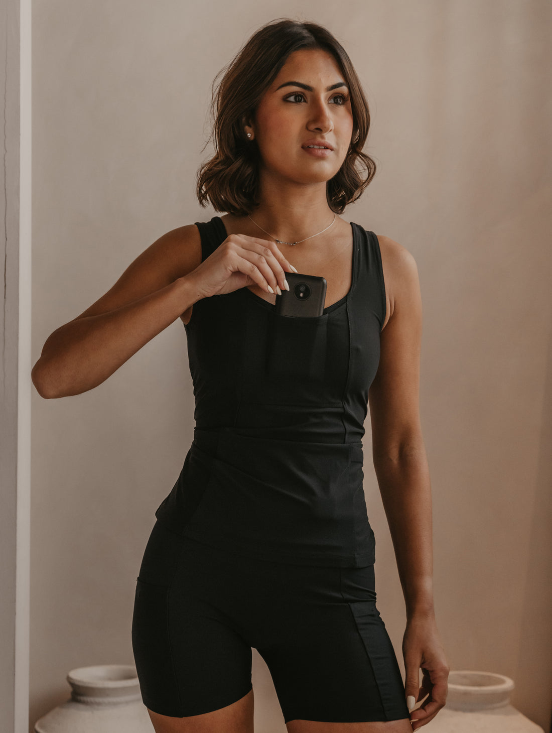 Woman wearing a black Mude Tank top and shorts, holding an Omnipod controller in the front chest pocket.