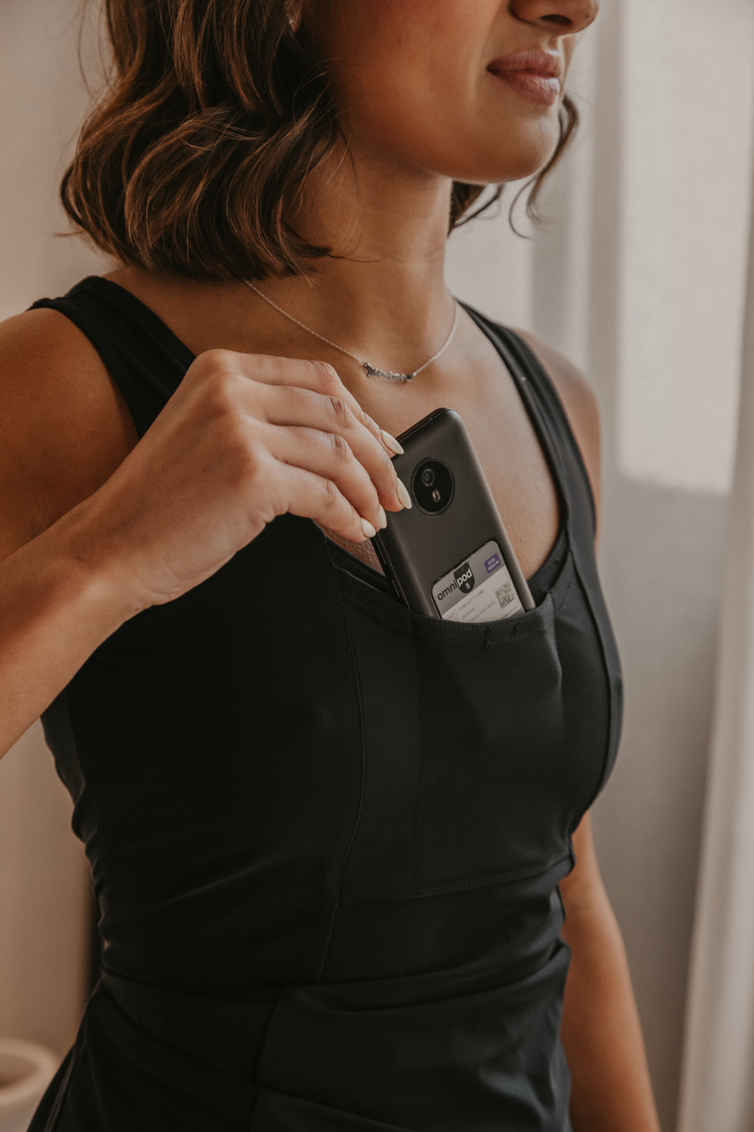 Woman holding an Omnipod controller in her black Mude Tank top with a blurred background