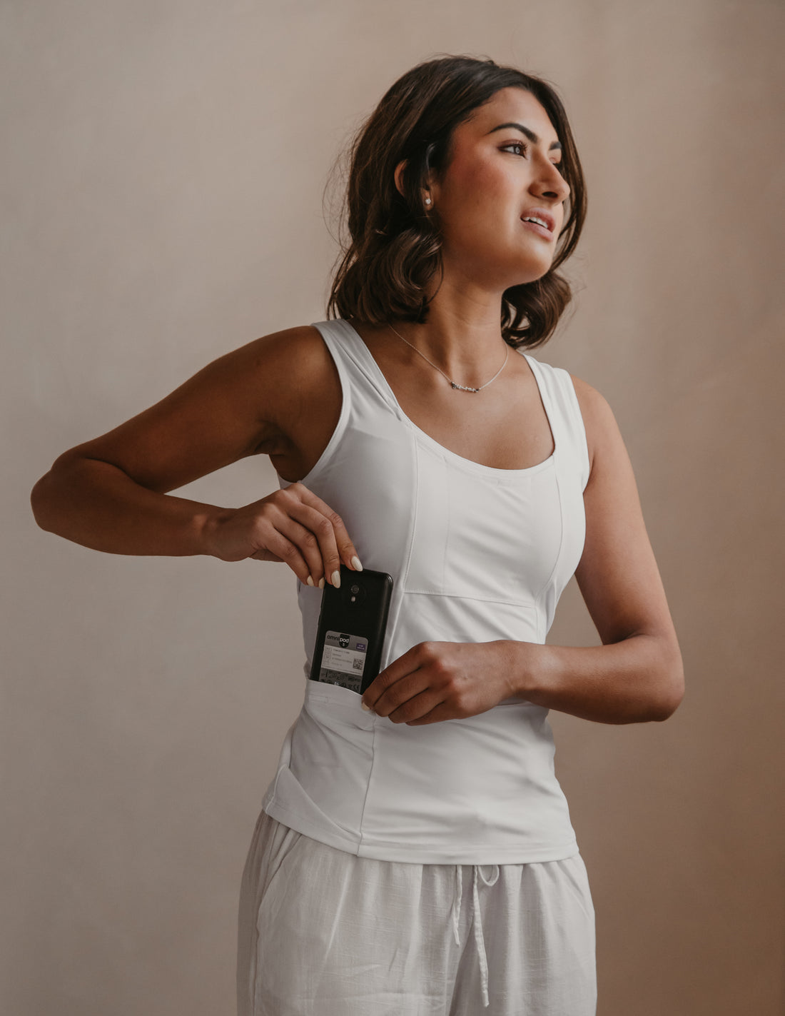 Woman wearing a white Mude Tank top and light grey pants against a beige background
