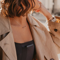 Woman wearing a beige trench coat over a black Mude Tank top with a blurred background