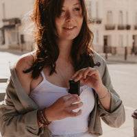 Woman placing an insulin pump into her white Mude Camisole top outdoors with a blurred background.